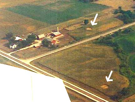 The top arrow points at corn circle measured 46 feet, 5 inches in diameter near Coon Hunter Road, Blue Grass, Iowa. On August 22, 1991, farmers Delmar and Carol Meyer found that circle of corn swirled counterclockwise. Three days later on August 25, 1991, a local pilot (deceased Blue Grass mayor) flew over and found the second circle near old Highway 61, now called 140th Avenue.  That counterclockwise circle also measured 46 feet in diameter. Aerial image courtesy Carol and Delmar Meyer.