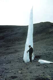 One of the last remnants of Kilimanjaro's Eastern ice field is a six-meter spire that was much larger on previous expeditions. Ohio State University geologist, Lonnie Thompson, Ph.D., stands beside it in 2002. The tall sliver of ice will soon be gone as global warming temperatures rise. Images © 2002 by Lonnie Thompson.