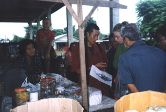 Mr. Lenoi of Phoudoi Travel Co., Vientiane, is showing "Briau Wildman" drawing to people in the market as Bang Productions Ltd. Associate Producer, Jax Hayes (glasses), listens. Photograph © 2001 by Linda Moulton Howe.