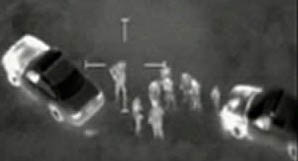 A FLIR video frame in which the hot engines of the two cars appear white. The rest of the cars are a much cooler black and grey, except for the "white hot" tail lights. Some people at the center have "white hot"heads and cooler grey, clothed bodies. Images courtesy www.FLIR.com.