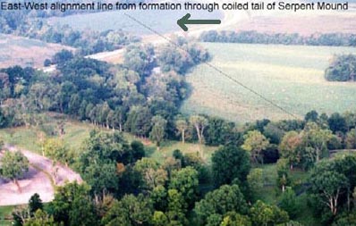 Arrow points at the soybean formation through early morning mist. Thin black line extends from the formation to lower right beige clearing which is the tail of the Serpent Mound.  Aerial photograph © 2003 by Jeffrey Wilson and Roger Sugden.
