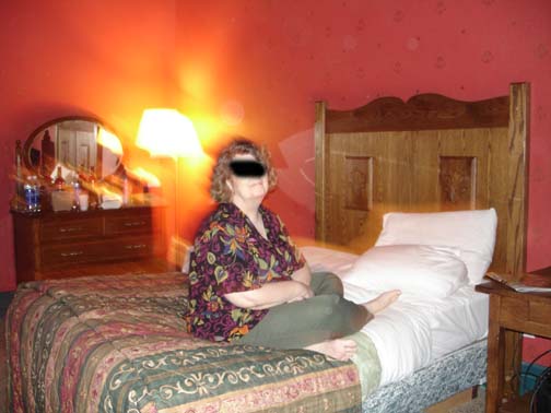 Above and below: Eureka Springs, Arkansas, Crescent Hotel room, February 2006. Photographer's sister's face blacked out at request. Behind the sister, the lamp and dresser objects seem to be in motion, as if a time lapse. Yet, the sister and foreground seem still. There is a "concentric" orb above the sister's head, which in the photograph below seems to have moved to the pillow. The translucent oval, or "fish" pattern, at the left of the high bed frame seems to move slightly. Images © 2006 by Susan Saffa. 