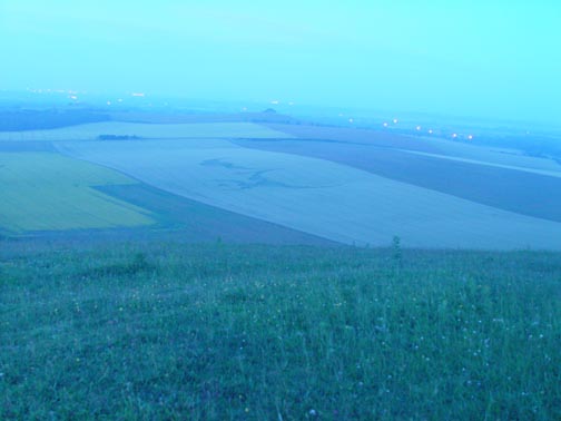 Approximately 3:20 AM, Saturday, July 7, 2007, Alton Priors, Wiltshire, England. Sony digital still frame in pre-dawn misty haze from atop Knap Hill looking toward Woodborough Hill (center dark clump of trees near horizon.) Vast wheat formation of 150 circles spread across 1,033 feet was created some time in the previous 90 minutes to hour and 45 minutes. Image © 2007 by Winston Keech.