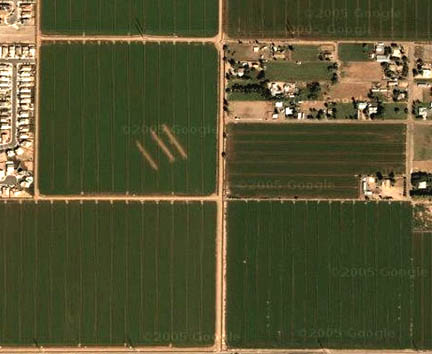 Google Map satellite photos above and below show three parallel long strips in upper left field. In lower right field, there are a series of "dots" along tramlines that are also unexplained. Below is close-up of parallel strips in satellite image.