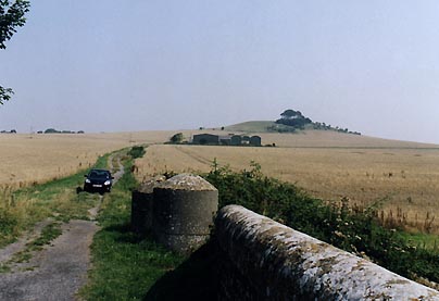 What Andy Buckley's perspective from the bridge would have been on July 14, 2003, when the black Apache helicopter was hovering low over the field to the right of the barns below Woodborough Hill. Photograph taken at approximately 11 a.m. in late July to show morning light conditions and the three faint marks in the field where Andy found the "bear claw" formation after the Apaches flew off on July 14, © 2003 by Linda Moulton Howe.