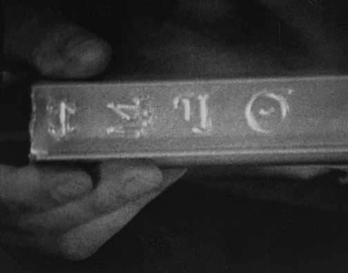 Photograph from another film segment of I-beam debris showing four more symbols: possibly Iota, Sigma, possibly Eta, Theta.