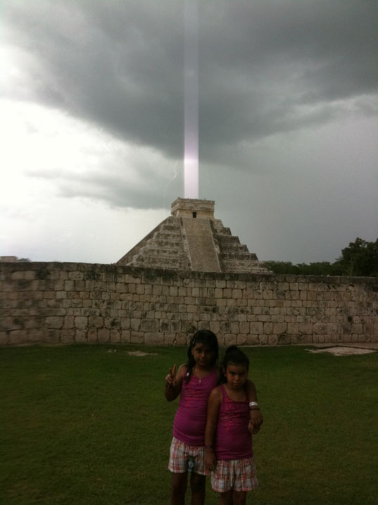 Apple iPhone photo that Hector Siliezar took on July 24, 2009, at 2:00:31 PM in front of the Mayan El Castillo (Kukulkan) pyramid at Chichen Itza as a thunderstorm began and lightning was captured to the left of the “beam.” Foreground left to right:  Stephanie Siliezar then 9 and Destiny Siliezar then 5.
