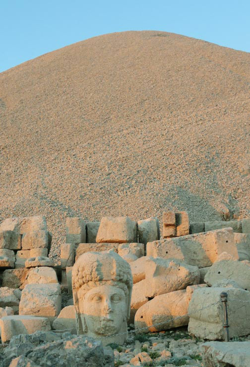 Mount Nemrut:  37° 58' 54.0012" N, 38° 44' 27.9996" E Mount Nemrut 25 miles north of Kahta, Turkey, and north of Gobekli Tepe, is another artificially covered mountain top above large stone heads of people and animals spanning cultures of Roman, Persian, Hellenistic, and Anatolian history. The artificial mountain top rises 164 feet above the carved statues that appear to have Greek-style facial features, but Persian clothing and hairstyling. Image © 2012 by Linda Moulton Howe.
