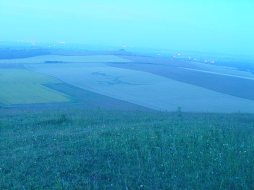 Approximately 3:20 AM, Saturday, July 7, 2007, Alton Priors, Wiltshire, England. Sony digital still frame in pre-dawn misty haze from atop Knap Hill looking toward Woodborough Hill (center dark clump of trees near horizon.) Vast wheat formation of 150 circles spread across 1,033 feet was created some time in the previous 90 minutes to hour and 45 minutes. Image © 2007 by Winston Keech.