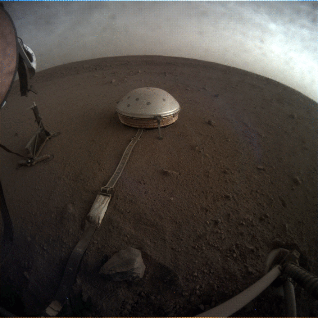 Martian clouds drift over the silver-grey and round seismometer known as SEIS that studies Martian seismic activity to reveal more about the Martian core. Moving gif image by NASA's InSight lander from October 1, 2019. Credit: NASA/JPL-Caltech.